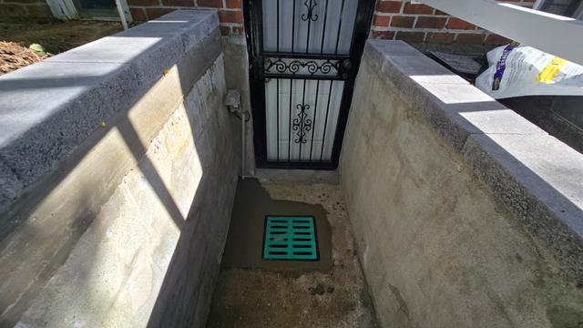 Areaway drain set between new concrete walls at a basement door