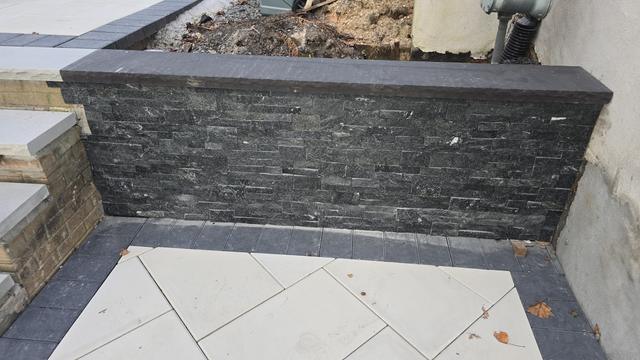 Black stacked-stone veneer wall with a smooth cap beside a light porcelain patio