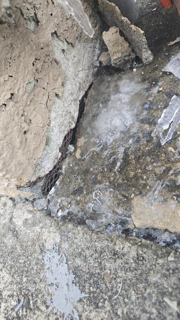 Close-up of broken, heaved concrete next to a foundation before repair