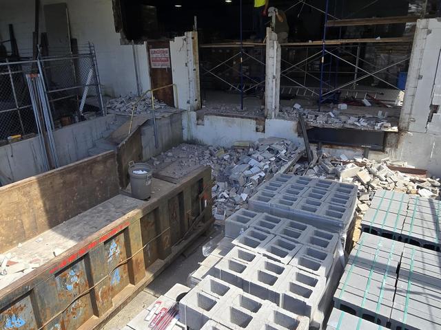 Pallets of new concrete masonry units staged beside a demolished wall