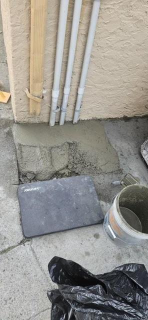 Concrete patch work at the base of a building wall with materials and a bucket nearby