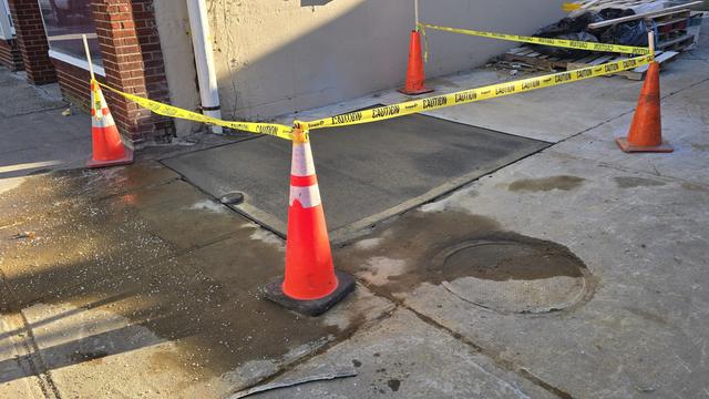 Repaired concrete area protected with cones and caution tape outside a building