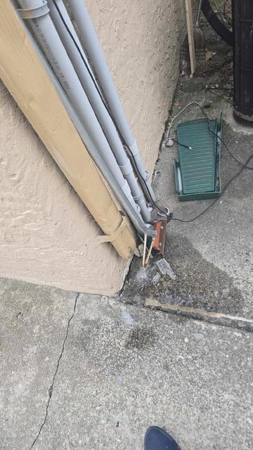 Cracked and settled concrete where utility conduits enter the ground beside a building