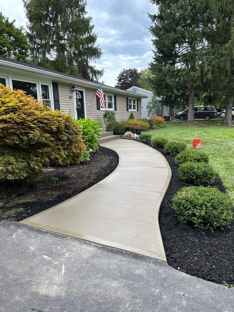 Curved broom-finish concrete walkway through a landscaped front yard with mulch beds and shrubs