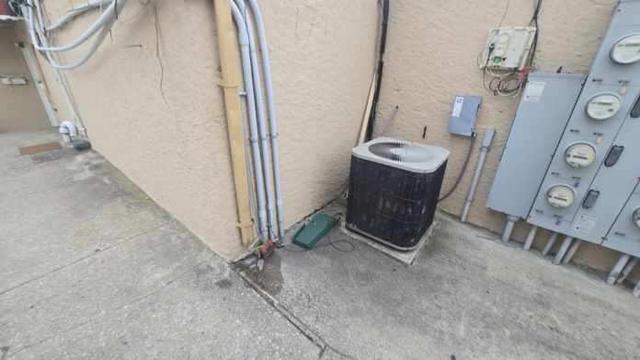 Worn concrete along the side of a stucco building near an AC unit and electric meters, before repair