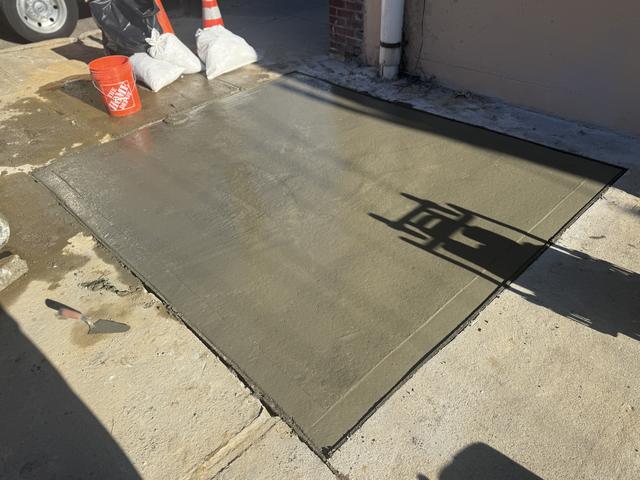 Freshly poured concrete slab with a broom finish beside a building, sandbags and cones around the work area