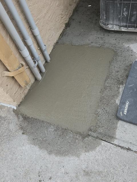 Freshly finished concrete patch around utility conduits at the base of a building