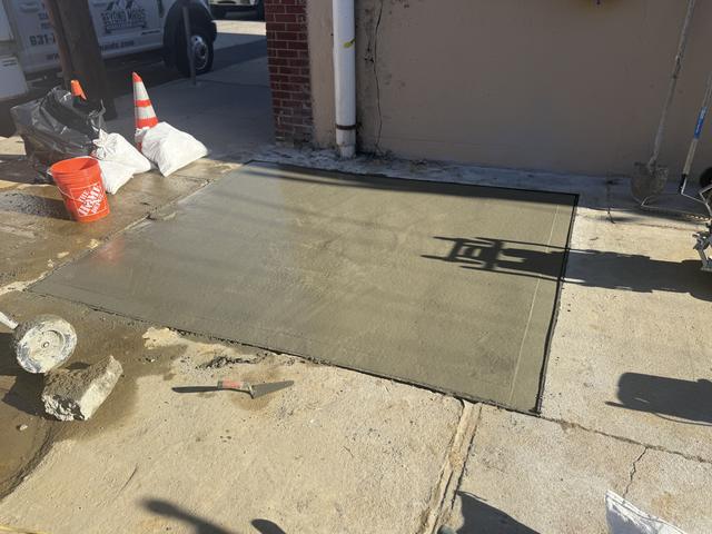 Fresh concrete slab beside a brick building, protected by cones and sandbags