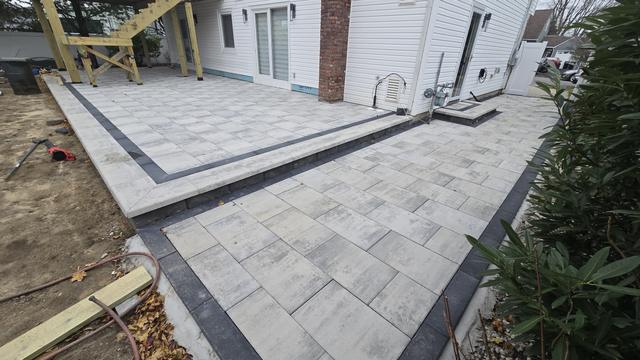 Gray paver patio with a charcoal soldier-course border along the side of a house