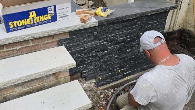 Mason installing dark stacked-stone veneer panels and caps on a wall