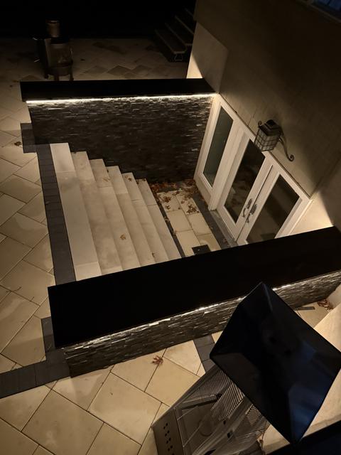 Below-grade stairwell at night with porcelain steps, dark stacked-stone veneer walls and LED strip lighting