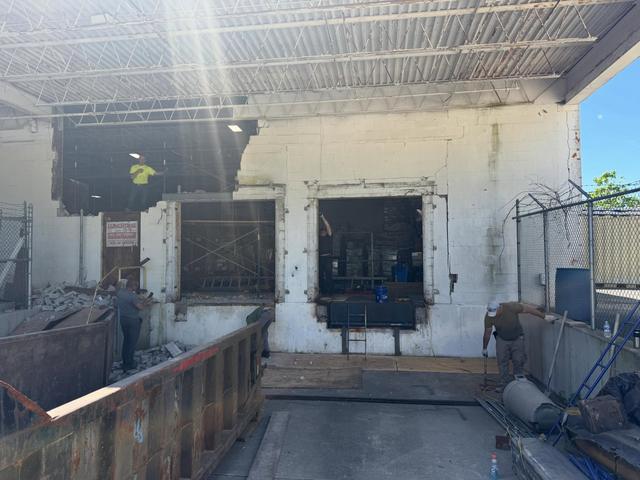 Commercial loading dock wall partly demolished, with scaffolding and debris containers