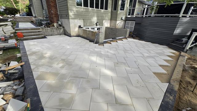 Backyard porcelain patio with a charcoal border next to a house and fence