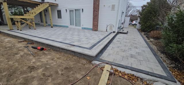 Porcelain patio under construction beside a house, with a dark border and walkway transition