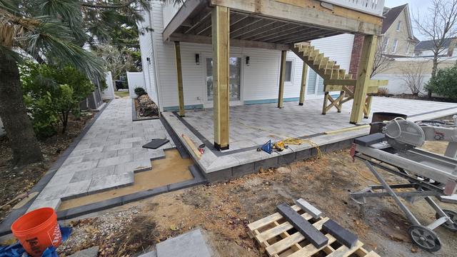 Large-format porcelain patio being laid under a raised deck, with the excavated base along the side