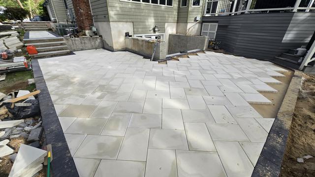 Porcelain patio installation in progress with a dark border, next to a house and deck