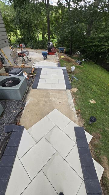 Light porcelain paver walkway with a dark border running down a side yard past AC units