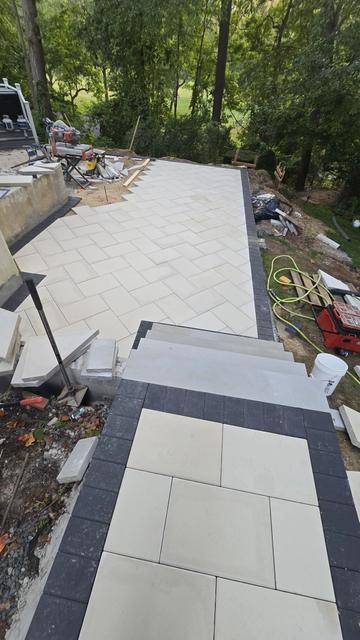 Large-format porcelain walkway with a charcoal paver border leading to wide steps in a wooded backyard