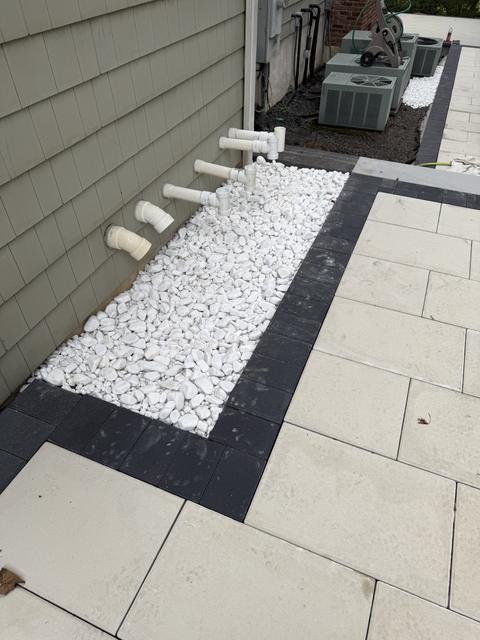 Porcelain paver walkway with a charcoal border and a white stone drainage strip along the house