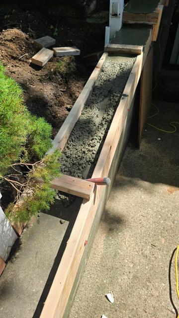 Concrete poured into forms for a new wall cap beside a walkway