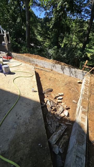 Excavated slope behind a house in a wooded yard, prepared for retaining wall construction