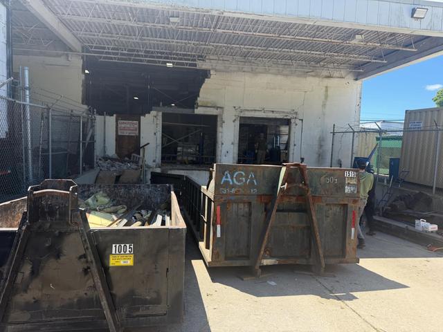 Dumpsters loaded with demolition debris in front of a commercial loading dock wall